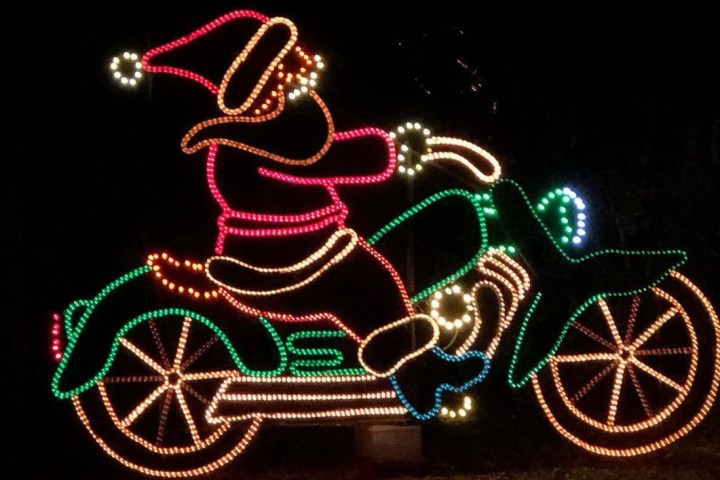 Neon lights outline Santa on a motorcycle against a dark background.