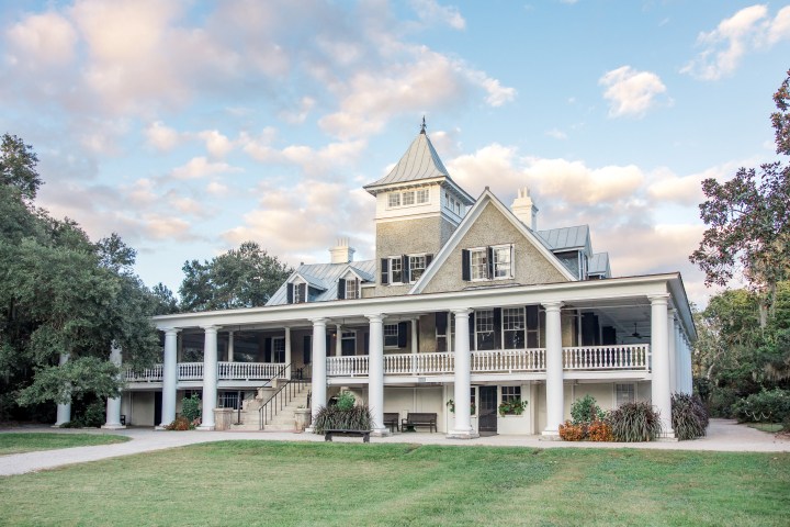 Historic plantation house with tall columns and large porch under a cloudy sky.
